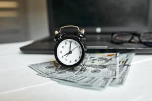 Modern workplace of laptop, clock, money, dollars banknote with copy space on white wooden background. Time for money. Will I Get Paid for Time Missed From Work Due to a Work Injury Concept