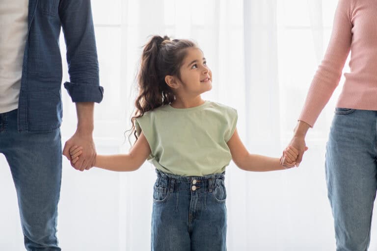 A Child holding onto both of her parents hands.